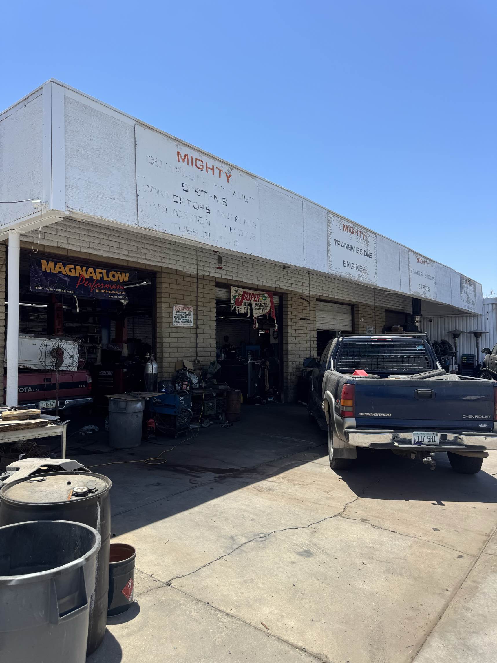 The Mighty Automotive Services shop front with open bays, a MagnaFlow banner, and a truck parked out front